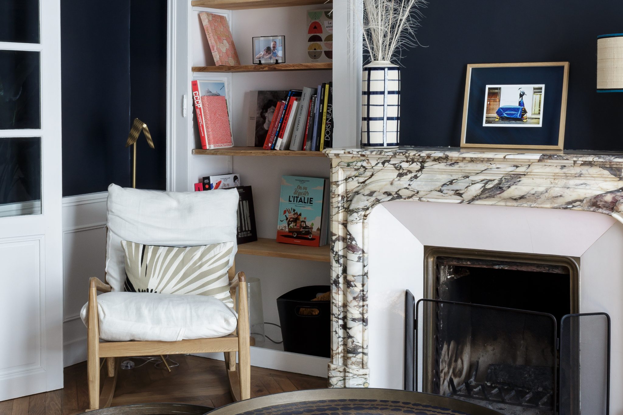 Salon aux murs bleu nuit avec cheminée en marbre, bibliothèque en niche et fauteuil en bois – Projet Mancelle au Mans
