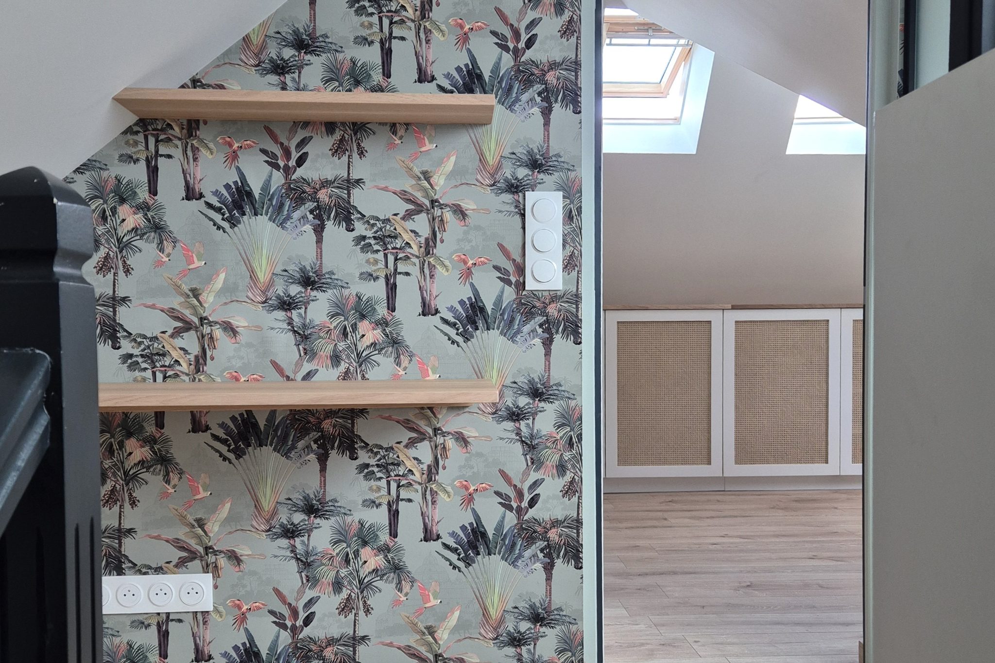 Palier des combles rénovés avec papier peint tropical, étagères en chêne et vue sur la chambre aux rangements cannés – Projet Marais au Mans
