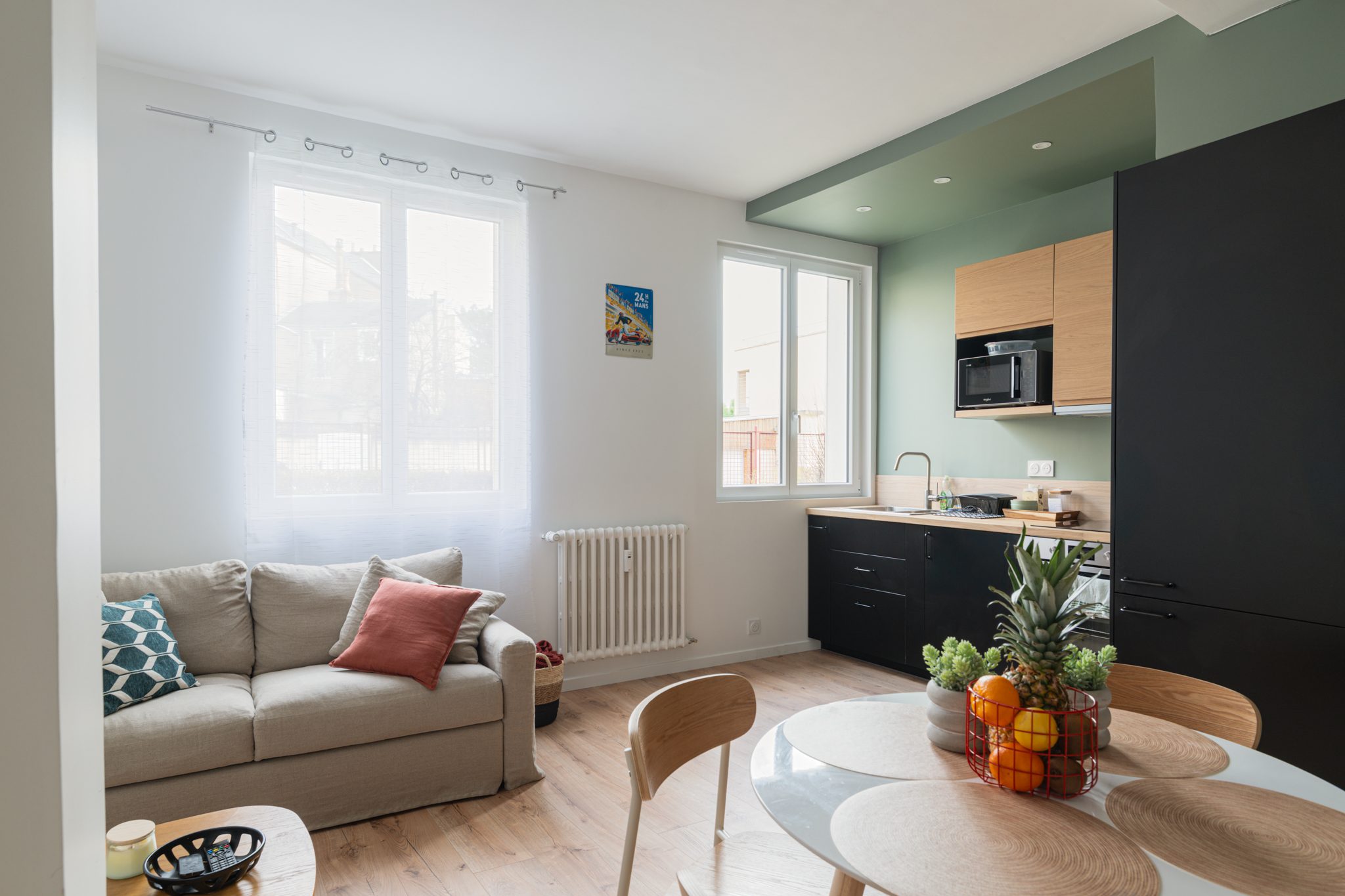 Séjour lumineux avec canapé en lin, cuisine noire et chêne sur mur vert de gris – Projet Ormeau au Mans