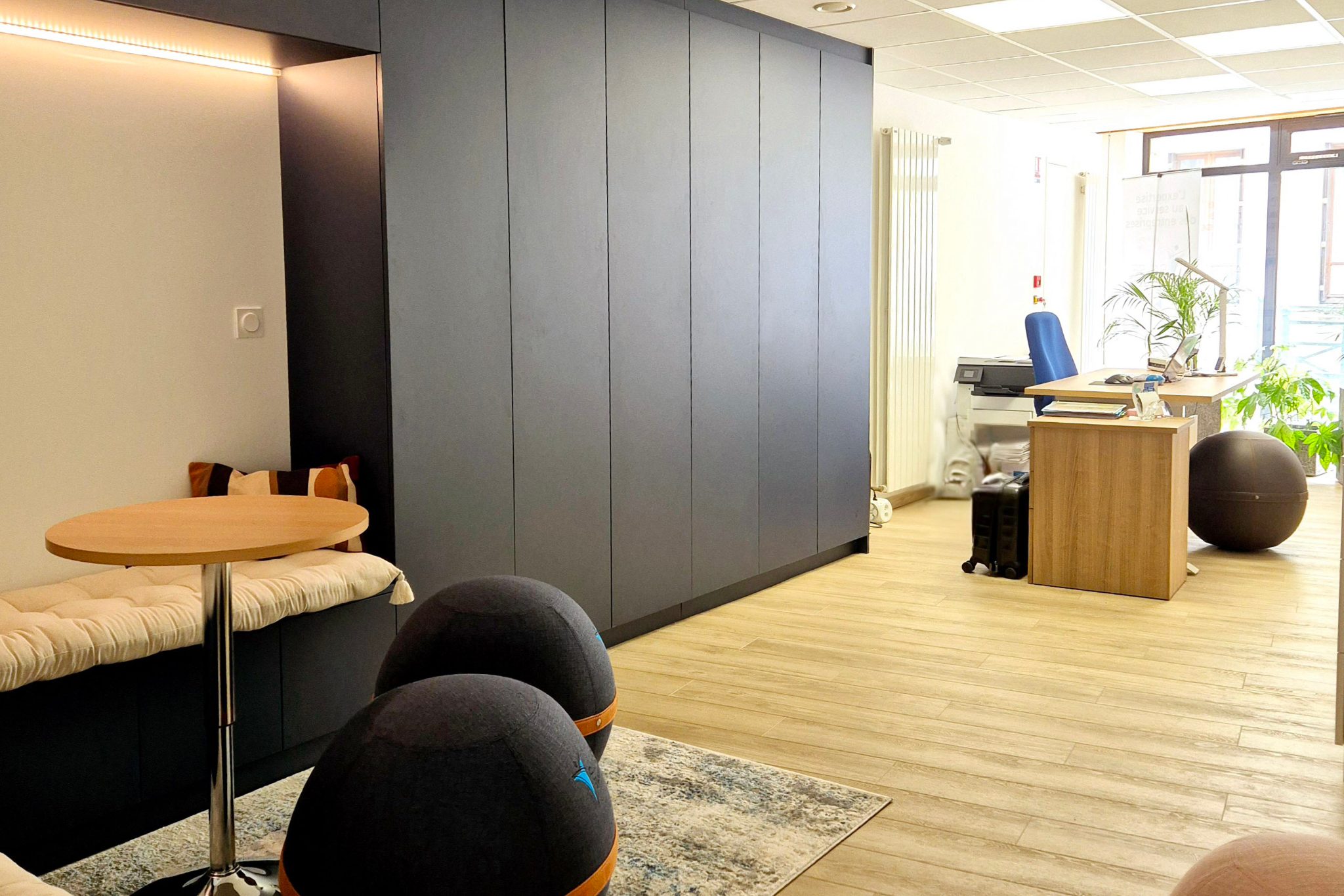 Local professionnel rénové : mur de rangements sur mesure bleu nuit, banquette intégrée et espace détente – Projet Vibraye au Mans
