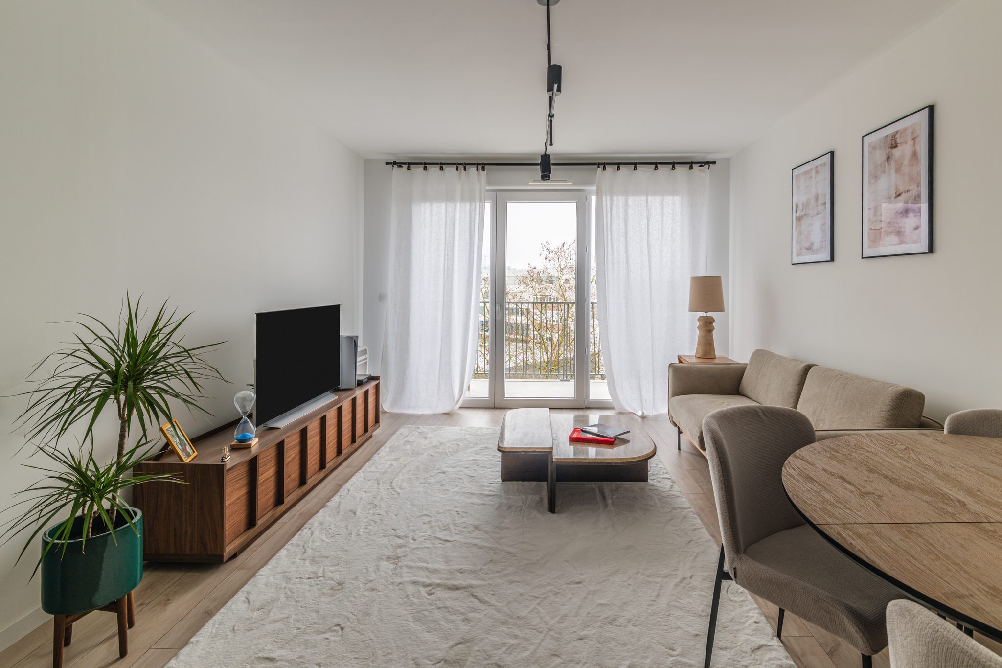 Séjour d’un appartement neuf décoré : meuble TV en noyer, canapé beige, table basse en bois et grand tapis blanc – Projet Washington au Mans